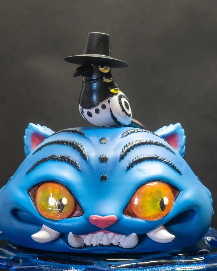 Figura pintada de un tigre azul de ojos naranjas con un pájaro de sombrero negro sobre la cabeza